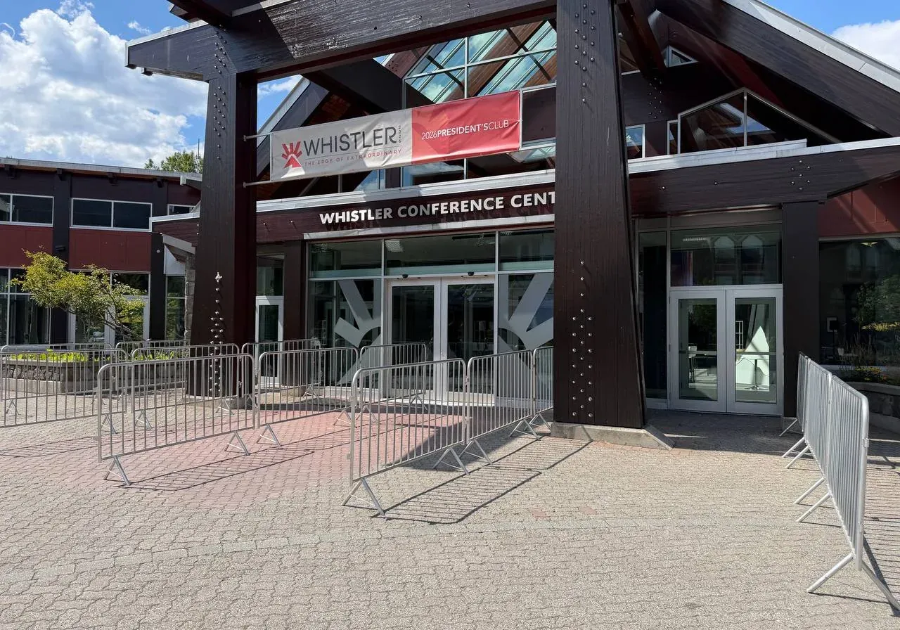 Galvanized steel crowd control barriers lined up across a paved forecourt outside a conference venue